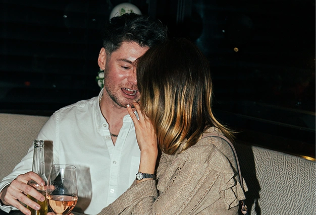 Man and woman in close conversation whispering and laughing over drinks (wine and beer) at a singles dating event.