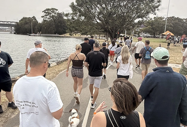 Diverse group of people walking along a waterfront pathway with a small dog during an outdoor social singles event or activity.